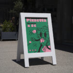 Caballete personalizado con un diseño creativo de una pizzería, situado en el exterior de un comercio.