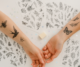 Dos brazos con tatuajes temporales en blanco y negro de flores, mariposas y aves, junto a varias láminas con diseños botánicos.